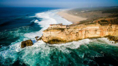 Cliffs overlooking a turbulent ocean under a clear sky.