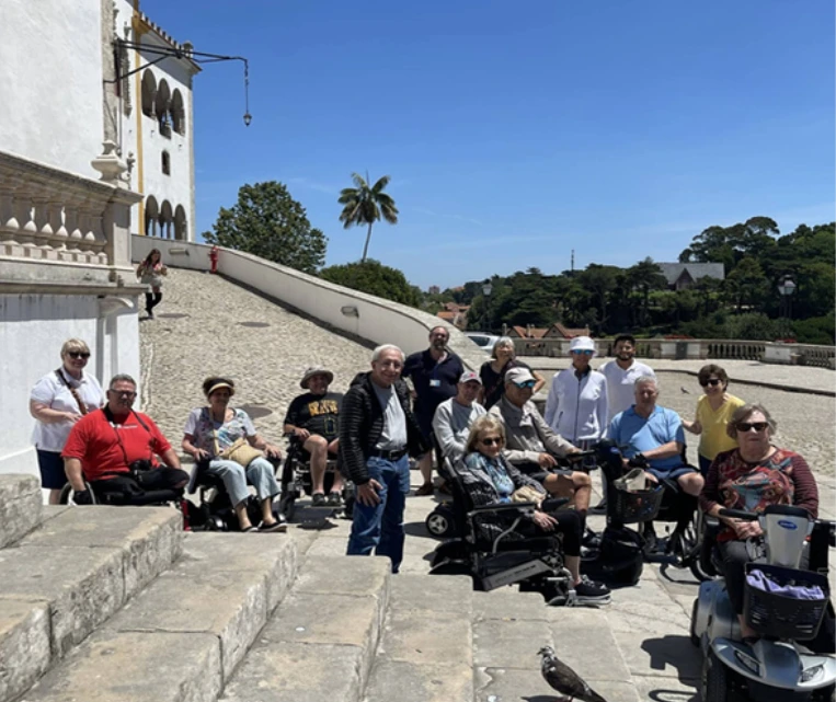 A group of people sitting and standing on stone steps by a river under a clear blue sky.
