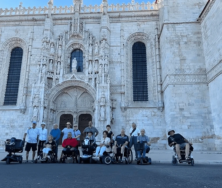 Group photo in front of a historic ornate building with people in wheelchairs.