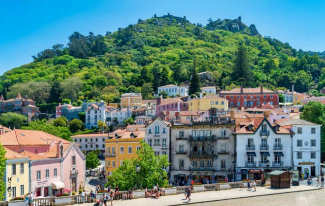 Colorful buildings at the foot of a green hill under a clear blue sky.
