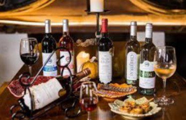 A variety of wine bottles and glasses set on a wooden table with food.