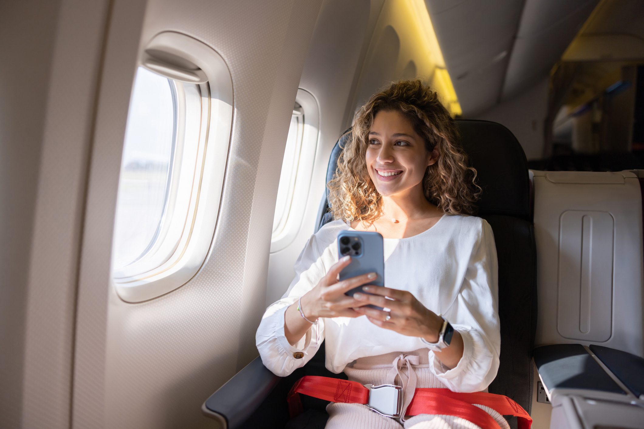 A woman smiling while using her phone on an airplane.