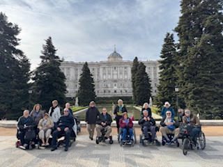 Group of people with strollers in front of a large building and trees.