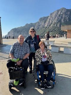 Three people smiling outdoors with mountains in the background.