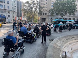 A group of people in wheelchairs gathered outdoors in an urban area.