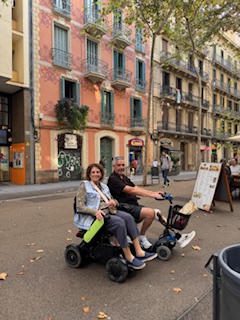 Two elderly people smiling while riding a mobility scooter on a city street.