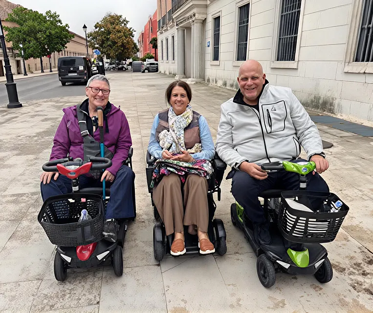 Three elderly people sitting on mobility scooters outside a building.