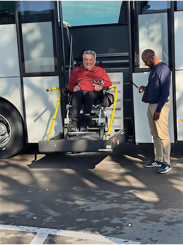 A man in a wheelchair descending from a bus with assistance.
