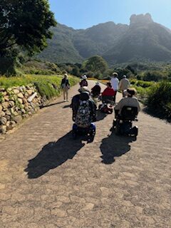 Group of people riding mobility scooters on a sunny path.