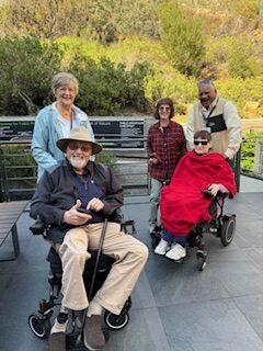Five elderly people posing outdoors on a sunny day.